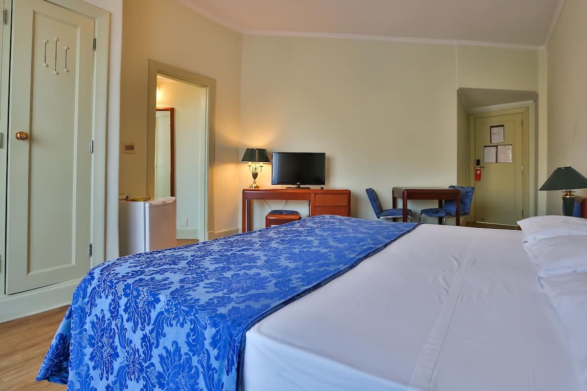 Une chambre d’hôtel comprenant un lit, un bureau avec une télévision, une chaise et une armoire.