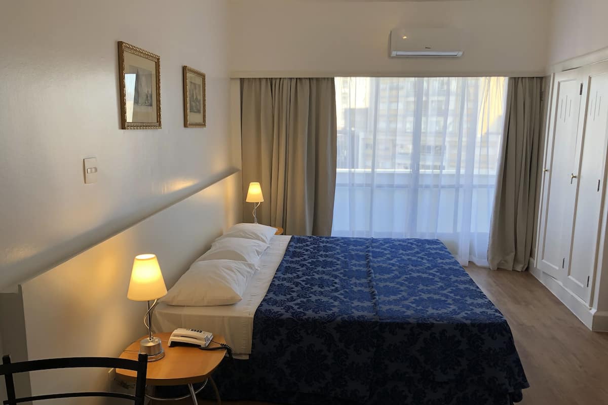 Une chambre d’hôtel avec un lit, des lampes de chevet, un téléphone, une chaise et une fenêtre avec des rideaux.