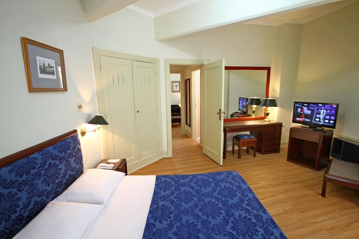Une chambre d’hôtel comprenant un lit, un bureau, une chaise, une télévision et une porte donnant sur une autre pièce.