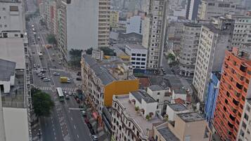 Paisagem urbana com edifícios altos, rua movimentada e área no terraço com mesas ao ar livre.