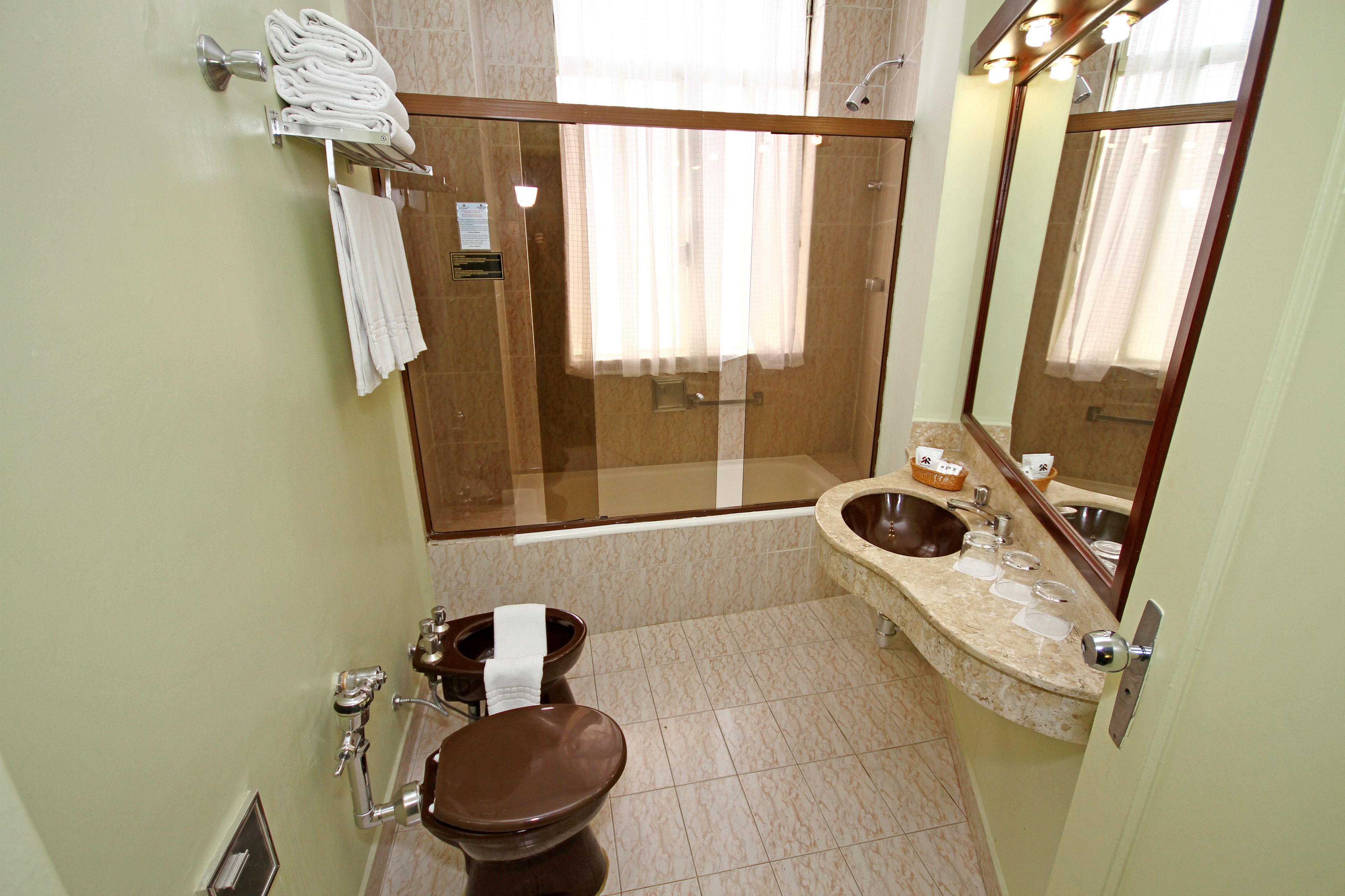A bathroom with a glass-enclosed shower, a toilet, a sink with a mirror, and towels on a rack.