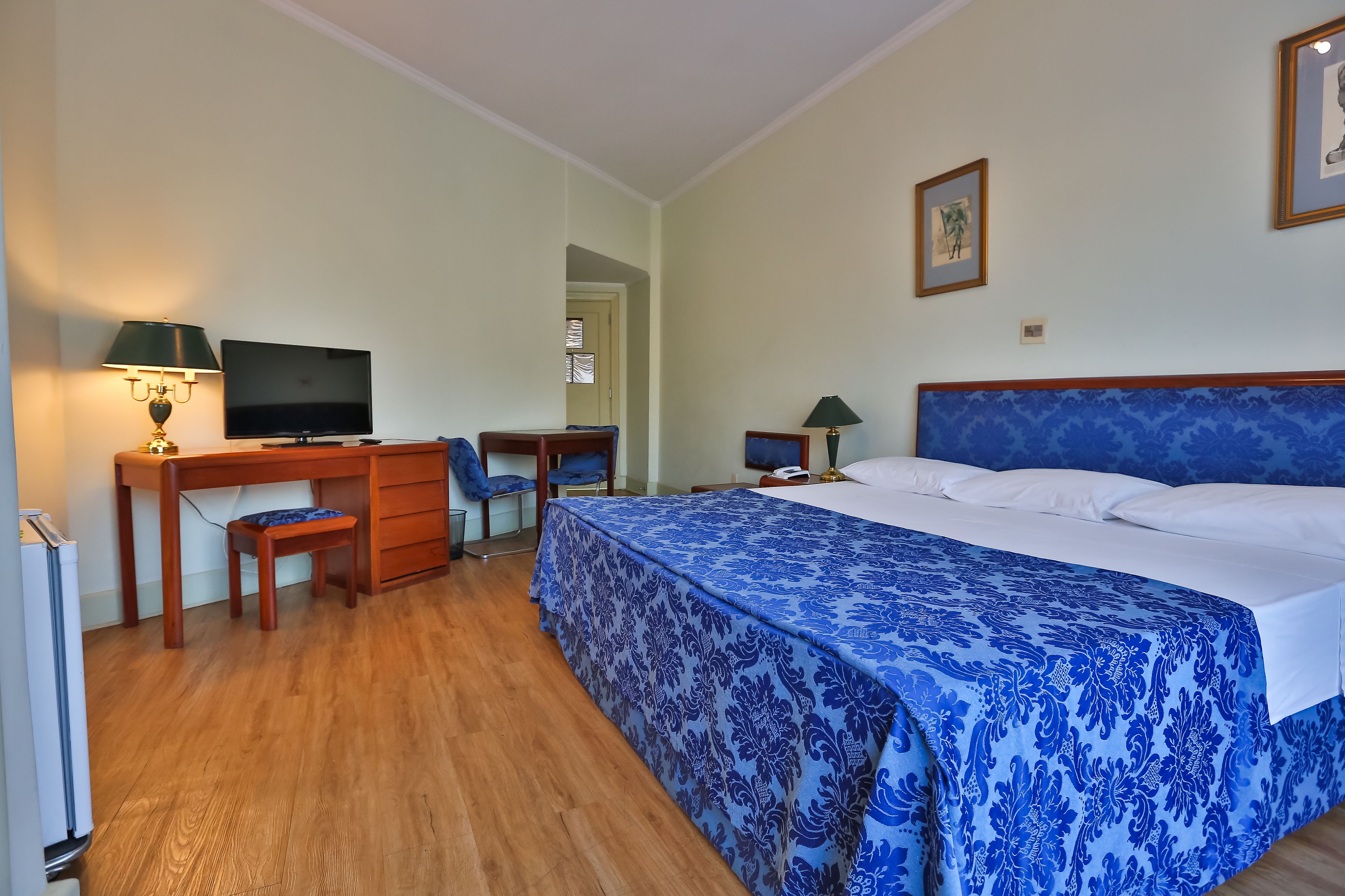 A hotel room with a bed, a desk, a chair, a television, and a lamp.