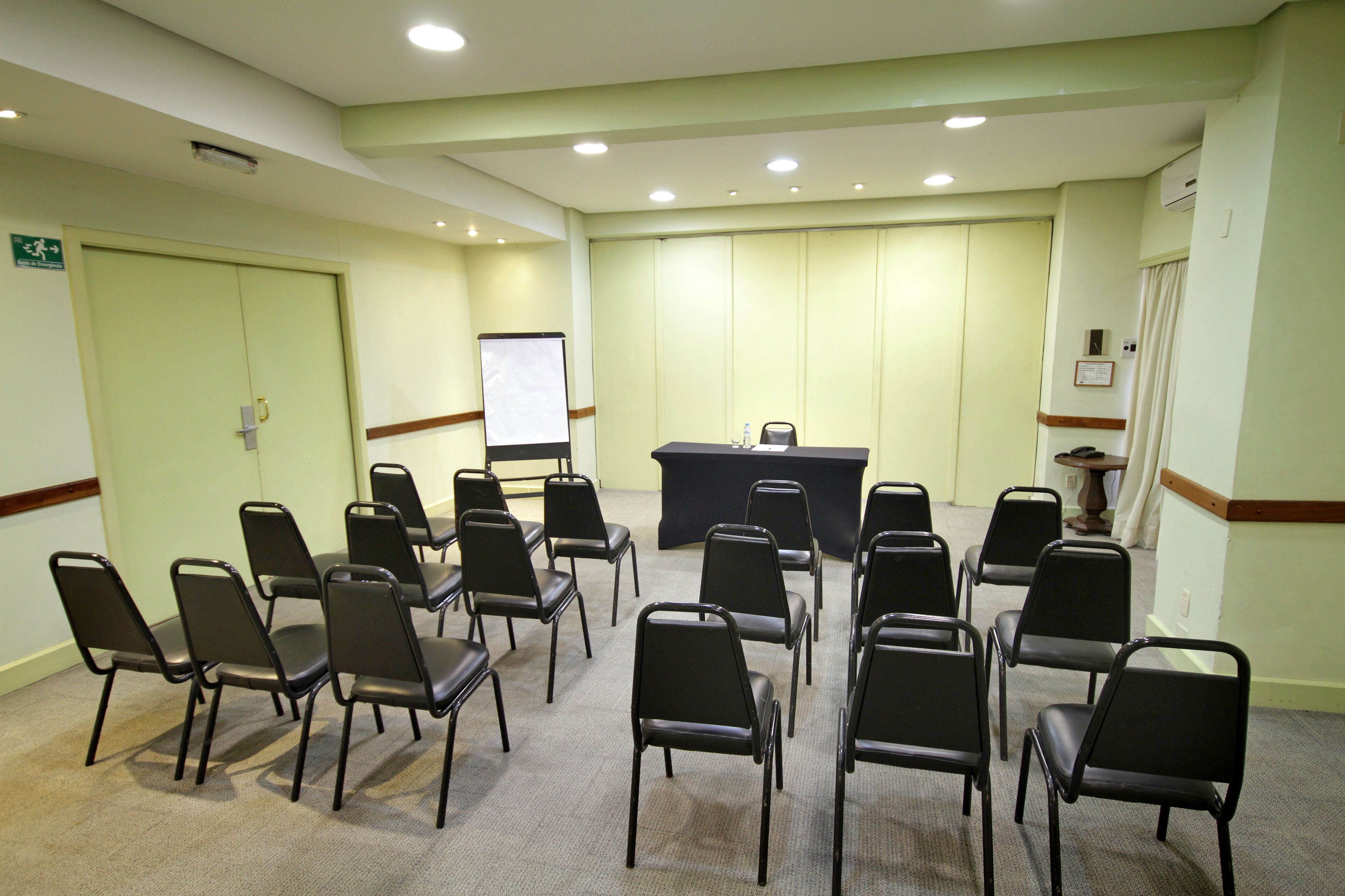 Un salón de conferencias con una mesa negra, varias sillas, una pizarra y un atril.