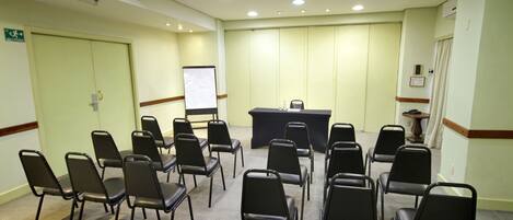 Un salón de conferencias con una mesa negra, varias sillas, una pizarra y un atril.