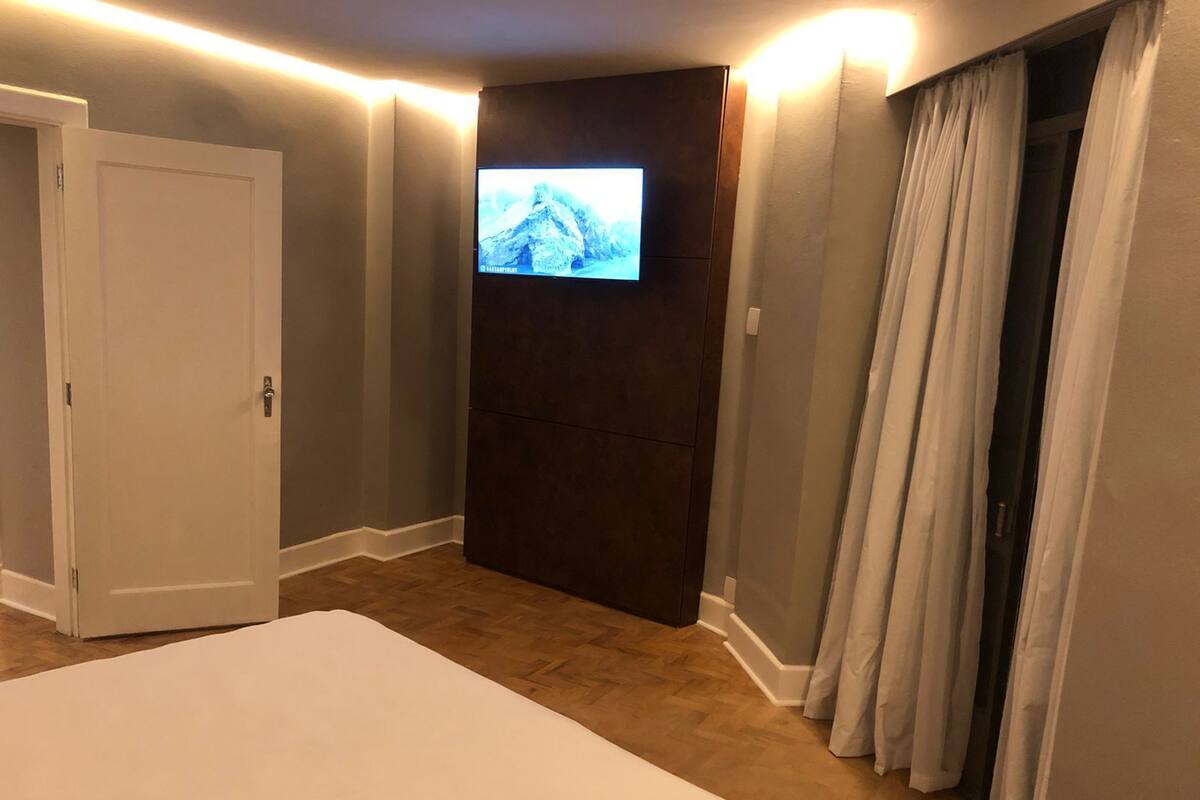 Une chambre d’hôtel avec un grand lit, un téléviseur à écran plat fixé sur un panneau sombre, une porte et une fenêtre avec des rideaux.