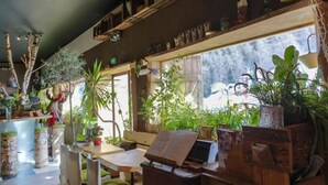 A cozy cafe with wooden furniture, a piano, and various plants. - Hôtel Green Ecolodge (Valdeblore)