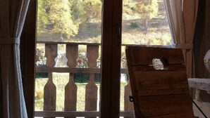 A room with a wooden chair and a window overlooking a forested area with a wooden deck. - Hôtel Green Ecolodge (Valdeblore)