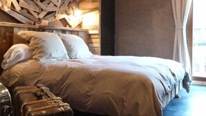 A bedroom with a bed, pillows, a headboard with wooden logs, a suitcase, and boots on the floor. - Hôtel Green Ecolodge (Valdeblore)