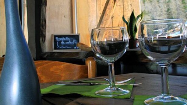 A wooden interior with a table set for two, featuring two wine glasses and a vase with branches. - Hôtel Green Ecolodge (Valdeblore)