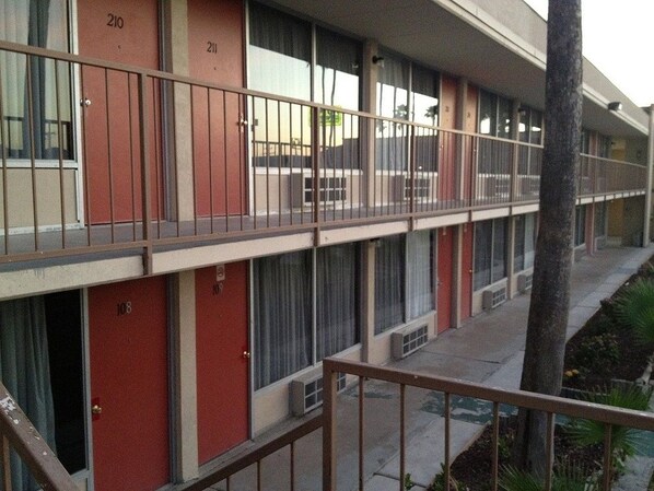 A multi-story motel with numbered rooms, a balcony, and a small garden area.