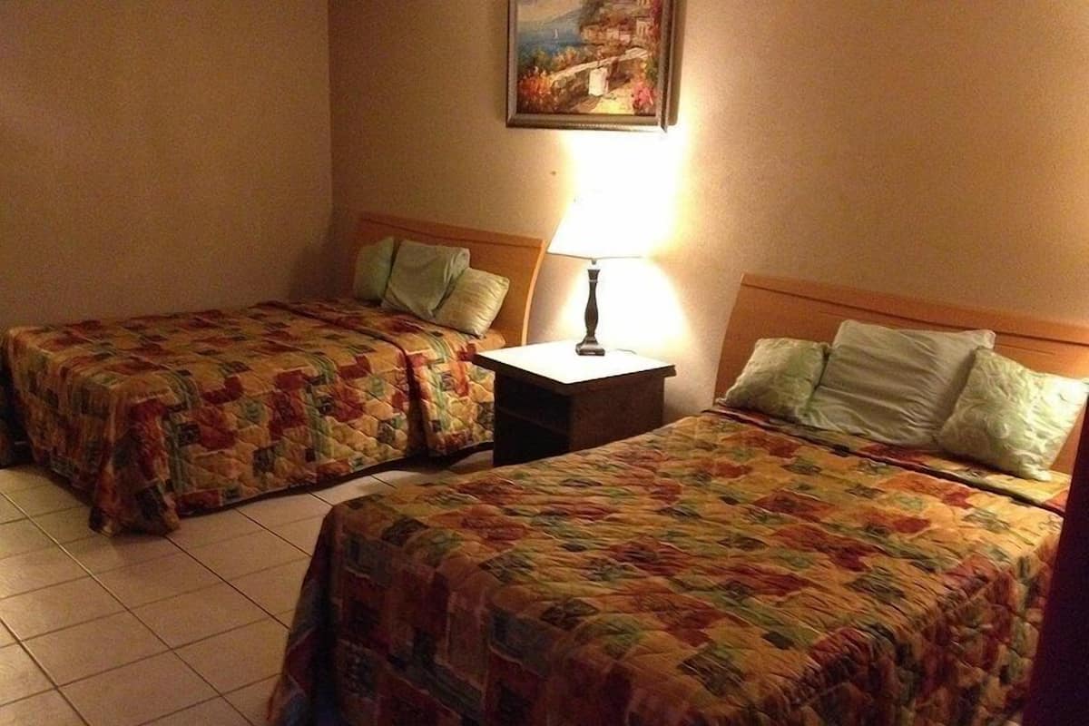 A hotel room with two single beds, a nightstand with a lamp, and a painting on the wall.