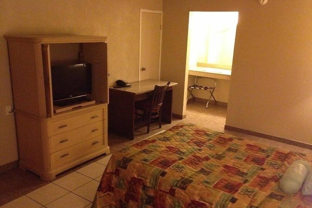 A bedroom with a bed, a desk, a chair, a television, and a window.
