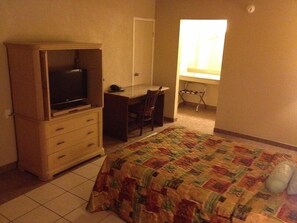 A bedroom with a bed, a desk, a chair, a television, and a window.