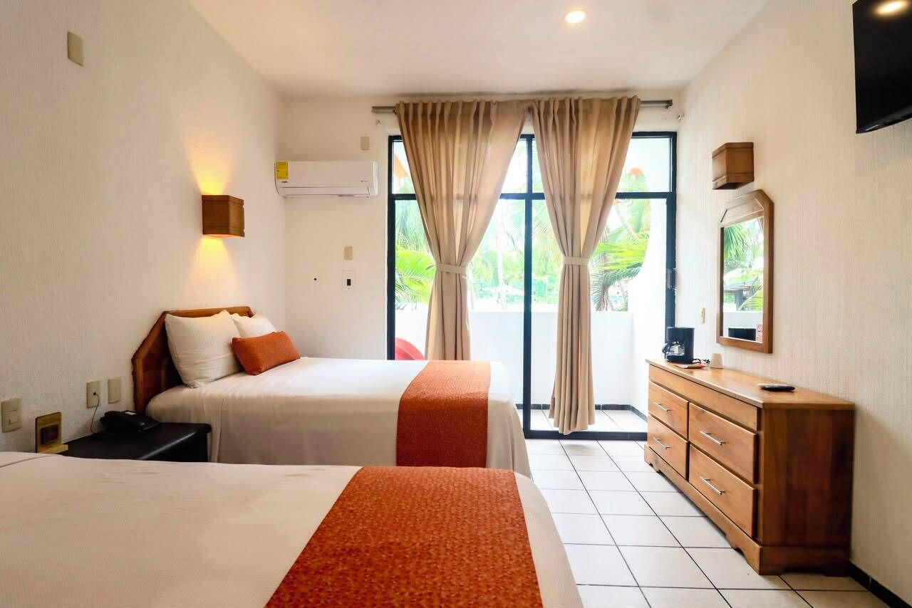 Habitación de hotel con dos camas, un aparador de madera, un televisor y un ventanal con cortinas.