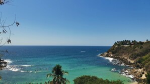 A coastal landscape with clear blue waters, a sandy beach, and rocky cliffs. - Hotel Surf Olas Altas (Puerto Escondido)