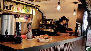 A café counter with a coffee machine, a menu board, and a sign reading "Vostal Café". - Hotel Surf Olas Altas (Puerto Escondido)