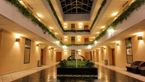A hotel lobby with a central planter, tiled floors, and a ceiling with a skylight. - Hotel Surf Olas Altas (Puerto Escondido)