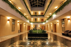 Un vestíbulo de hotel con una planta central, pisos de baldosas y un techo con tragaluces.