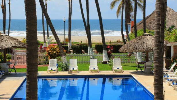 A pool with lounge chairs, palm trees, and a view of the beach. - Hotel Surf Olas Altas (Puerto Escondido)