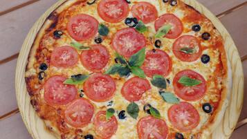 Pizza con rodajas de tomate, aceitunas y hojas de albahaca sobre una tabla de madera.