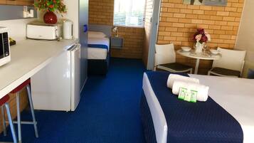 Habitación de hotel con cama, escritorio con microondas, pequeña mesa con un florero y una silla, además de ventana con vista a personas a lo lejos.