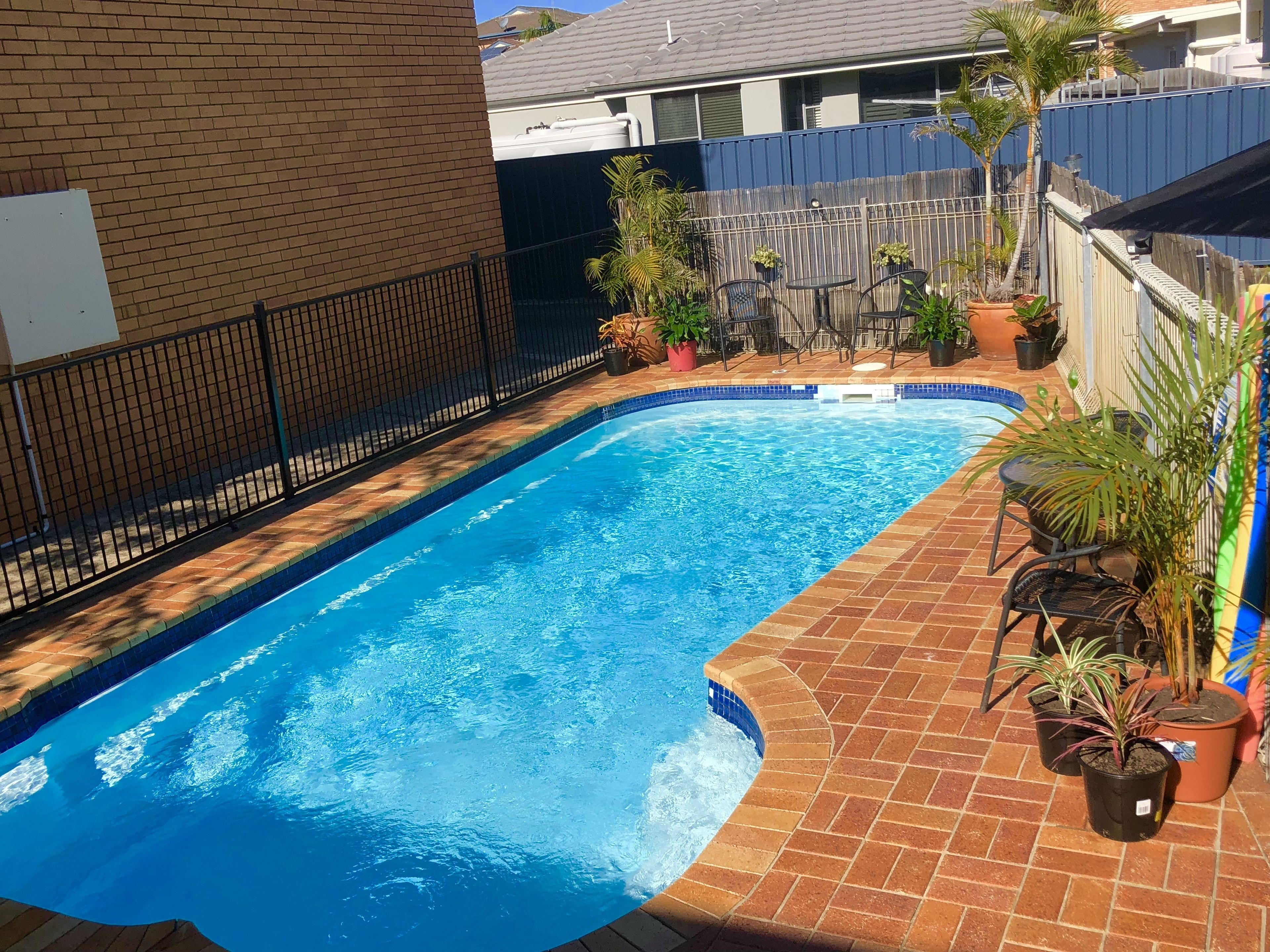 A rectangular swimming pool with a tiled edge, surrounded by a brick patio.