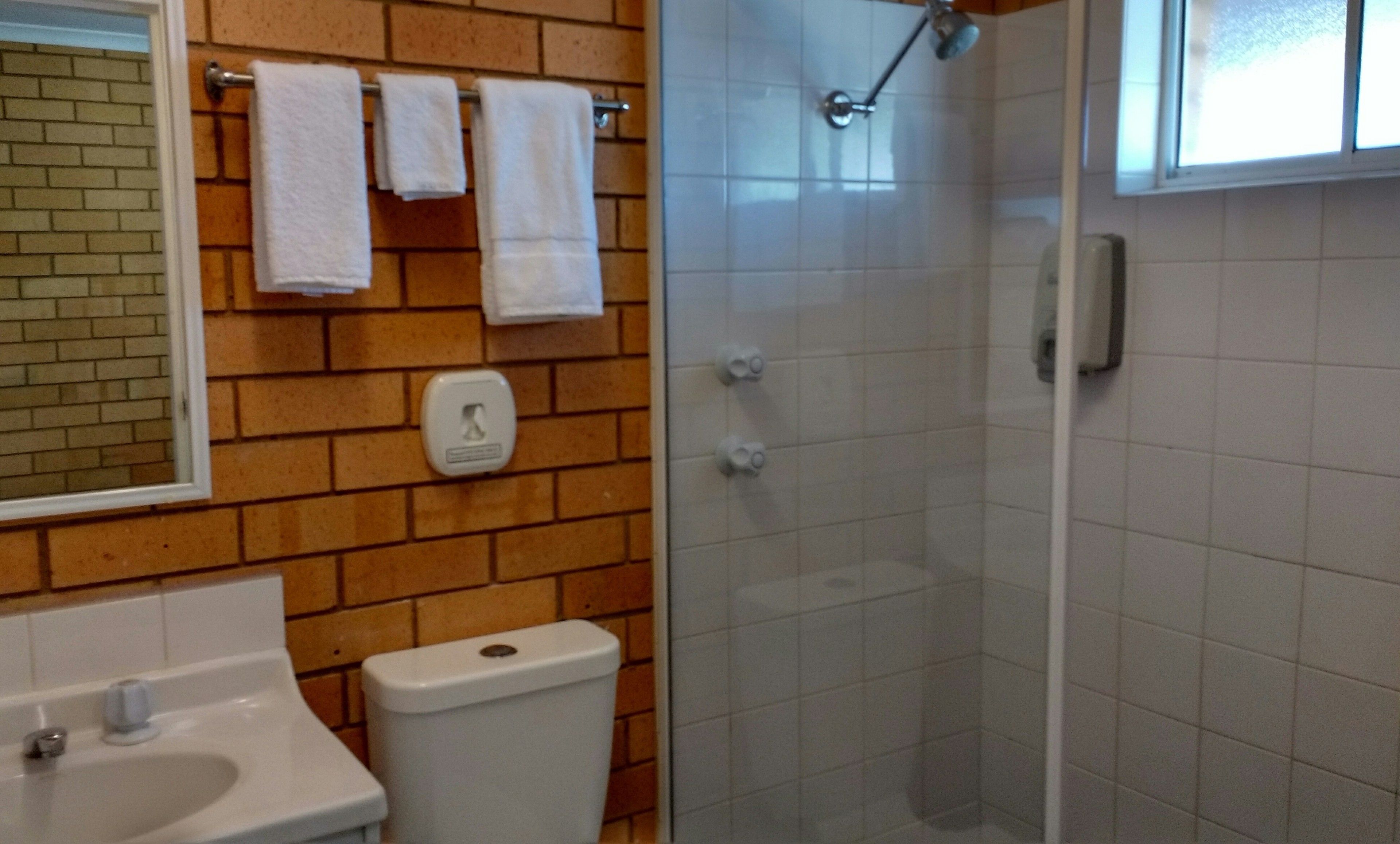 Un bagno con un lavandino bianco, un water e un box doccia in vetro. Asciugamani appesi a un portascopevoli sopra il water.
