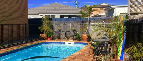 A backyard with a swimming pool, patio furniture, and potted plants.