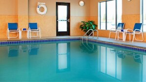 Piscina interna com água azul cristalina, cercada por espreguiçadeiras e plantas em vasos.