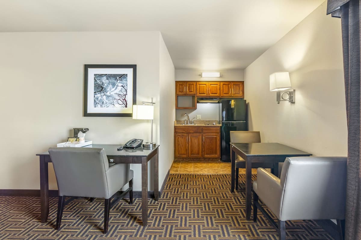 Une chambre d’hôtel avec un coin repas, une cuisine dotée de meubles en bois, d’un réfrigérateur et d’un tableau encadré au mur.
