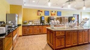 Um buffet de café da manhã com armários de madeira, uma ilha central e diversos pontos de serviço de alimentos.