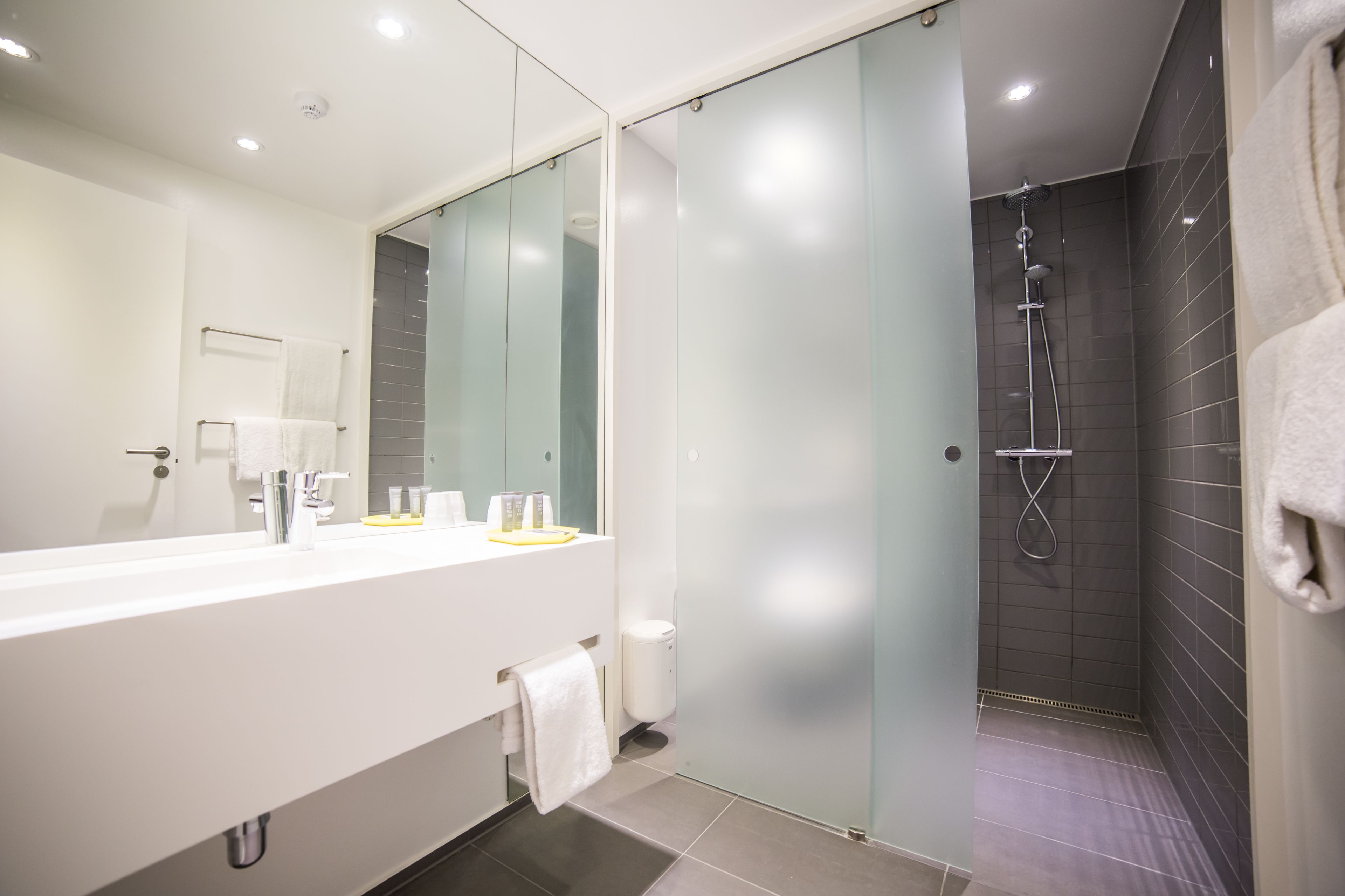 Un baño moderno con un espejo grande, ducha y un lavabo blanco.
