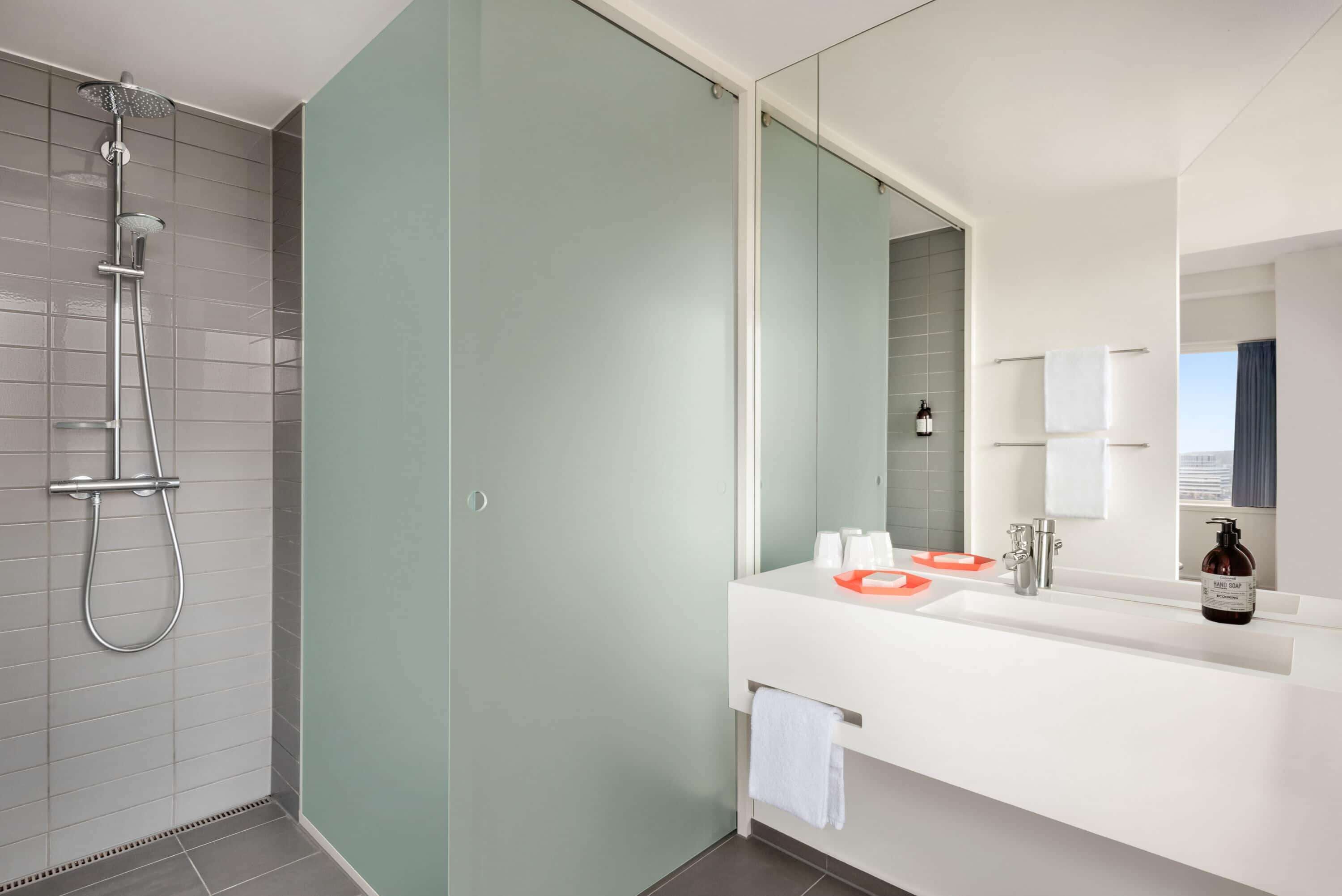 A modern bathroom with a shower, a large mirror, a white sink, and a towel rack.