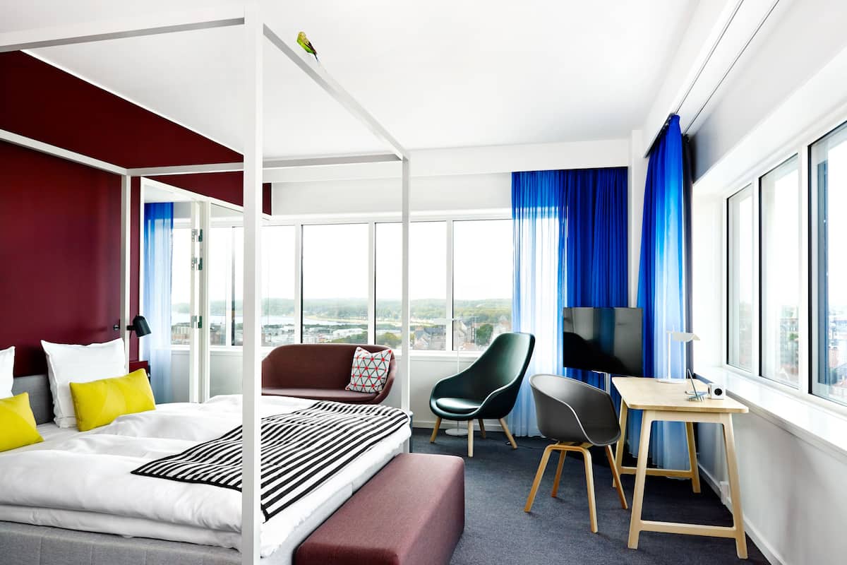 Een moderne hotelkamer met een groot bed, een bureau, een stoel en uitzicht op de stad.
