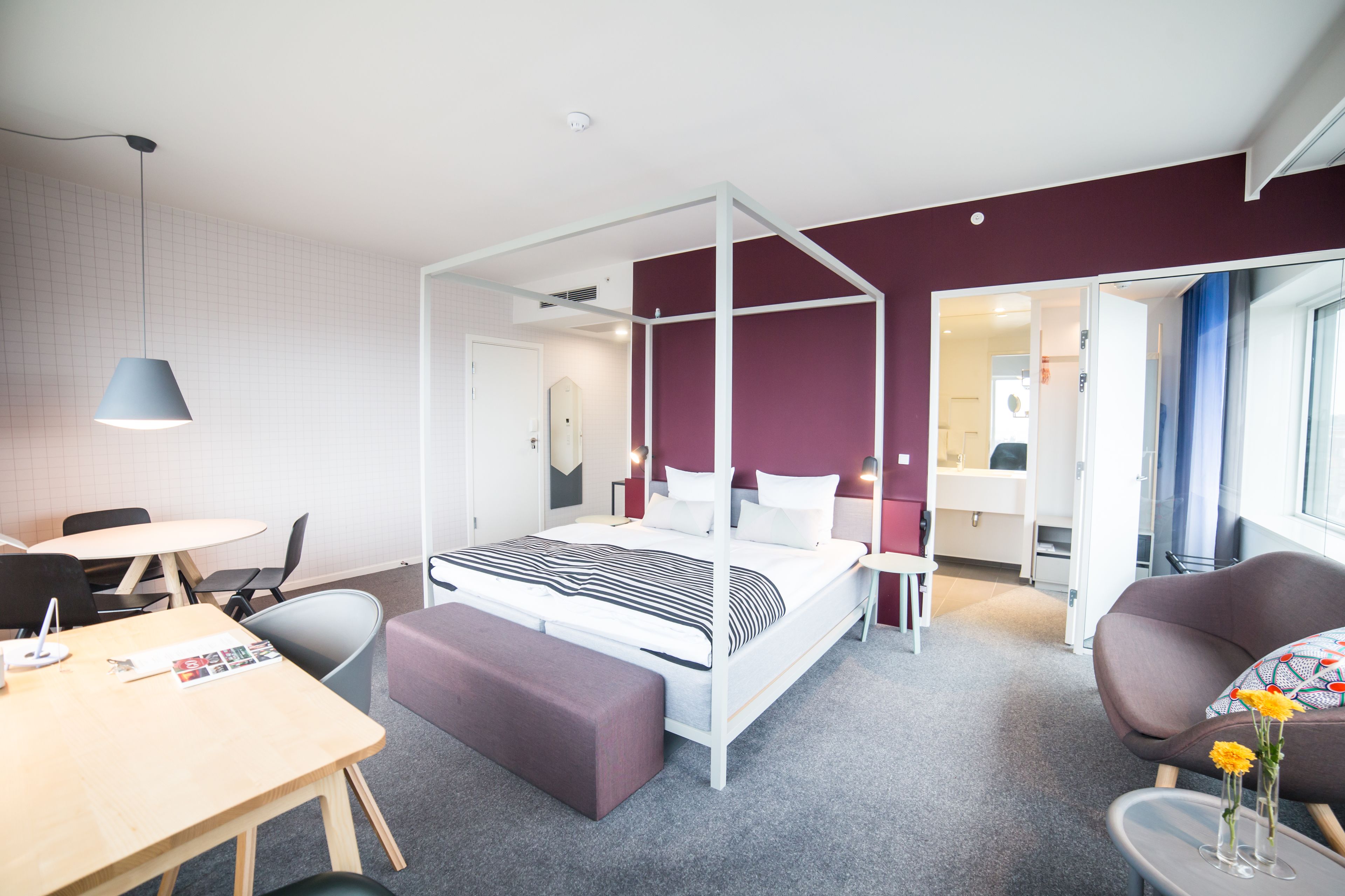 Una habitación de hotel moderna con una cama con dosel, un comedor y una zona de estar con vistas a la ciudad.