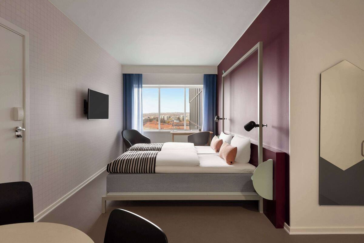 Een hotelkamer met een bed, een televisie, een bureau en een raam met uitzicht op de stad.