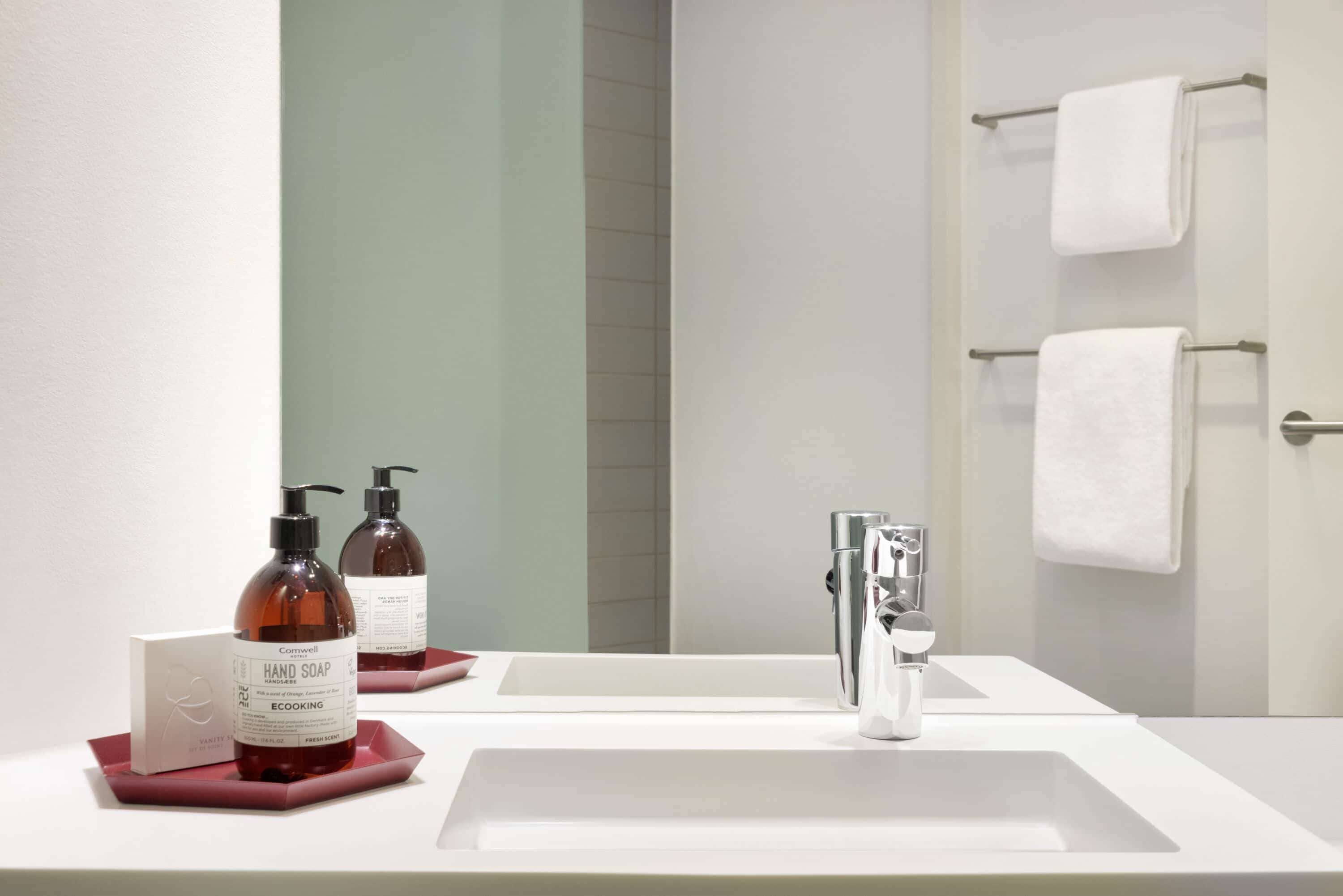 A bathroom with a white sink, two hand soap bottles, a mirror, and a towel rack.