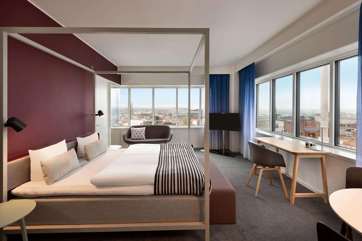 Een moderne hotelkamer met een groot bed, een bureau en uitzicht op de stad.