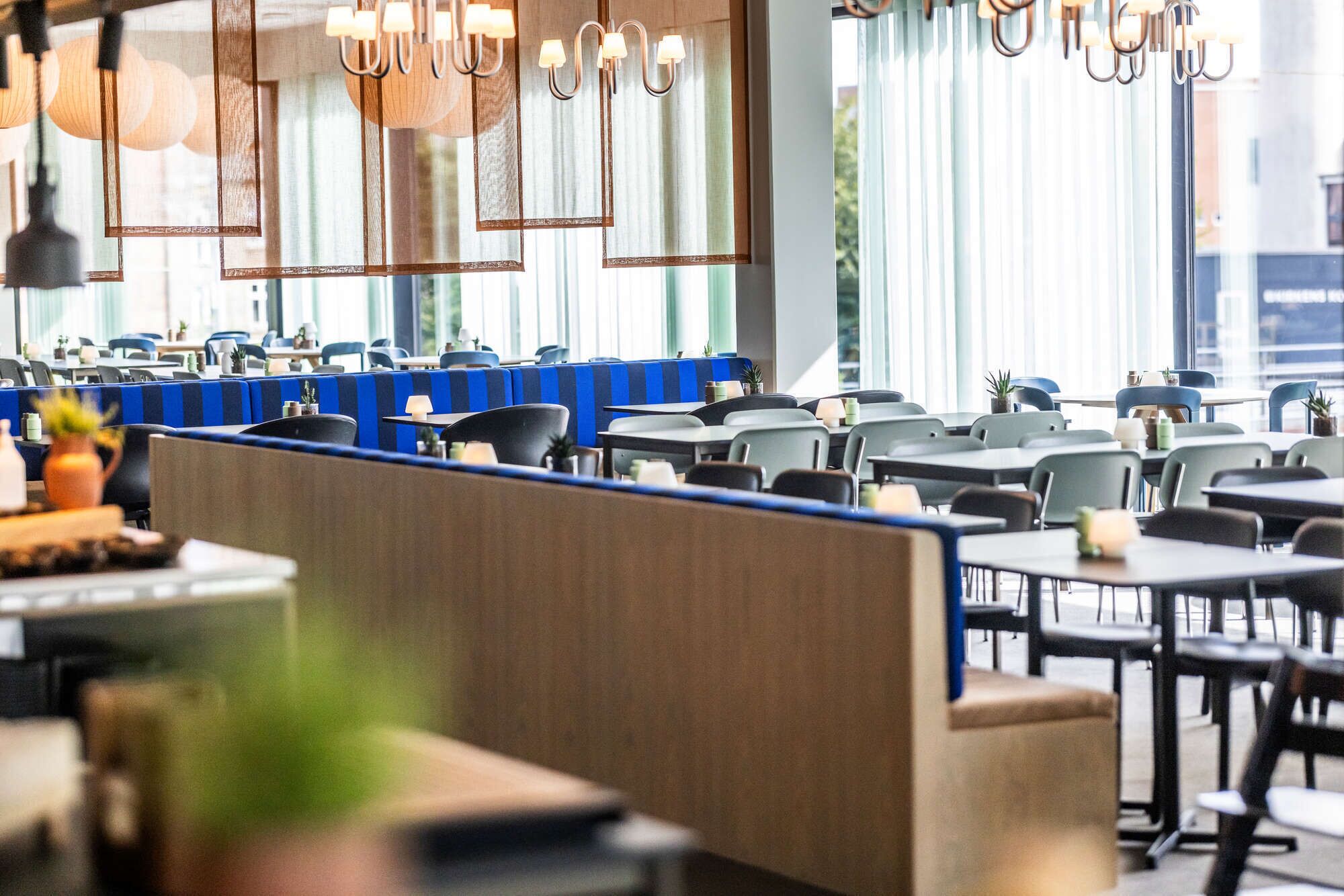 Un restaurante moderno con mesas altas, cabinas, ventanas amplias y lámparas colgantes.