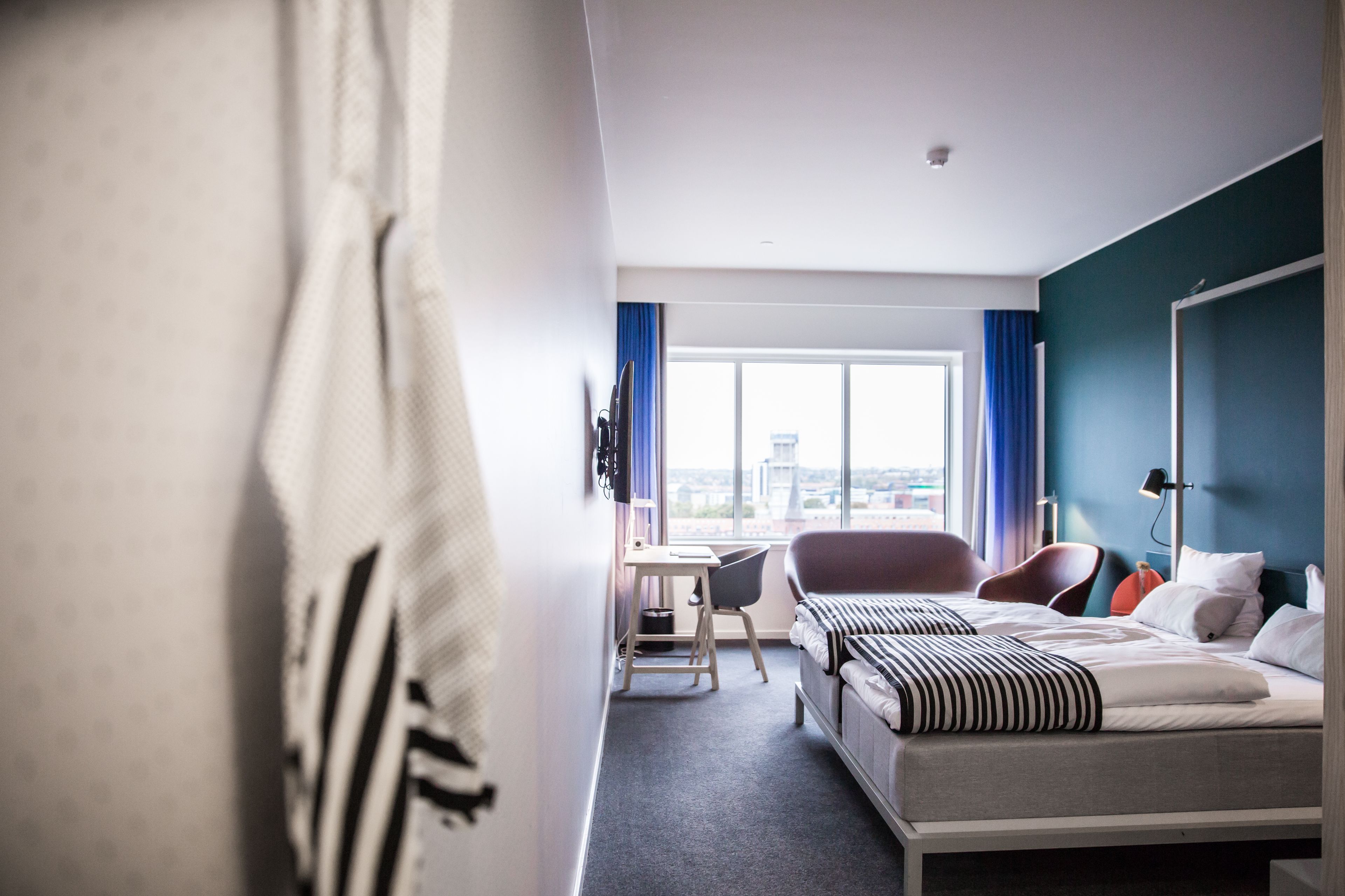 A hotel room with a bed, a desk, a chair, and a view of the city.