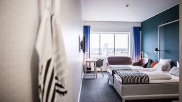 A hotel room with a bed, a desk, a chair, and a view of the city.