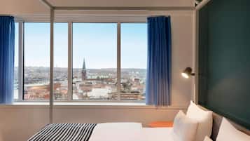 Et hotelværelse med et stort vindue, en seng, et sengebord og en lampe.