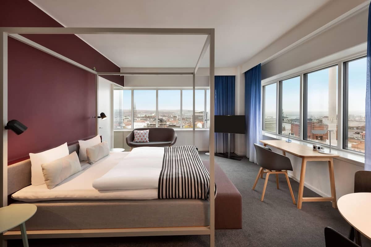 Een moderne hotelkamer met een groot bed, een bureau, een stoel en uitzicht op de stad.