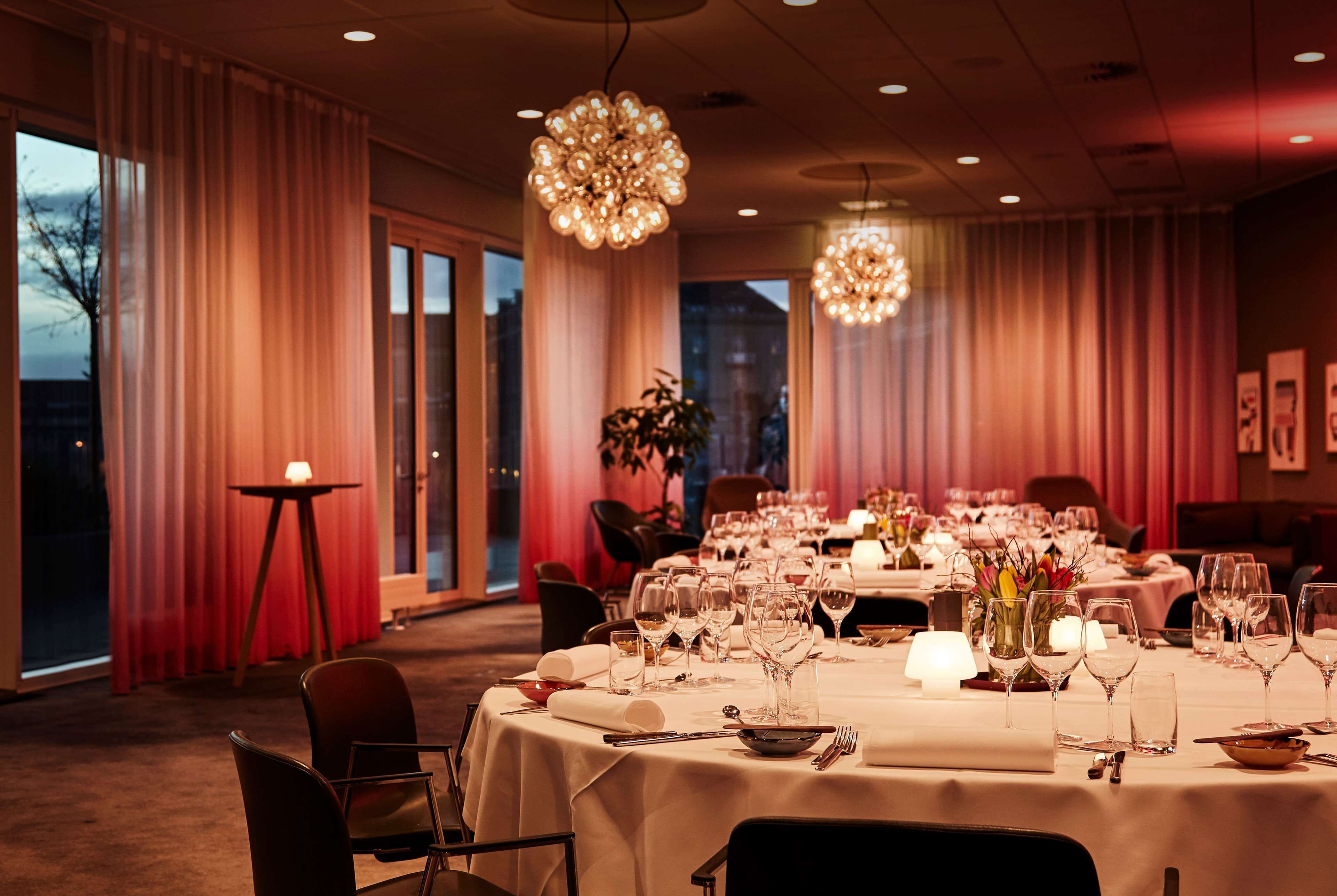 Une salle à manger élégante, avec une table dressée pour le repas, de grandes fenêtres et un lustre.
