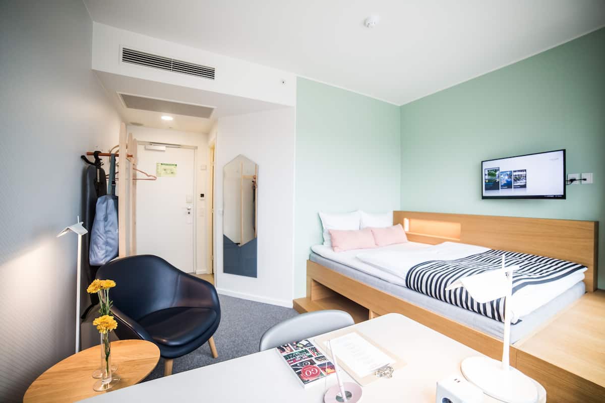 Een moderne hotelkamer met een enkele bed, een bureau met stoel, een klein tafeltje met vaas en een spiegel.