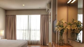 A hotel room with a bed, a desk, a mirror, and a window with curtains.
