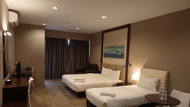 A hotel room with two beds, a desk, a chair, a small table, and a painting on the wall. - Hotel Primera Suite (Cyberjaya)