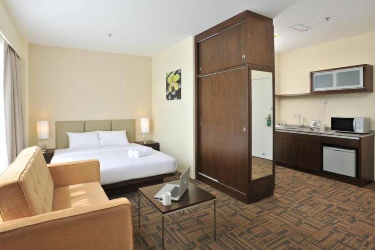 A hotel room with a bed, a desk, a chair, a microwave, and a small refrigerator.