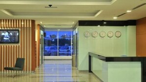 A hotel reception area with a TV screen, a reception desk, and clocks on the wall. - Hotel Primera Suite (Cyberjaya)
