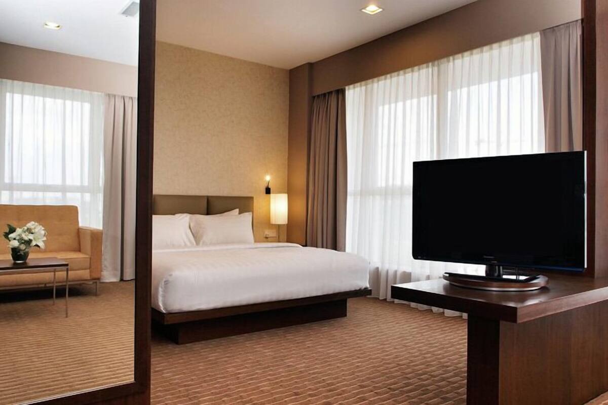 A hotel room with a bed, a TV, a sofa, and a lamp.